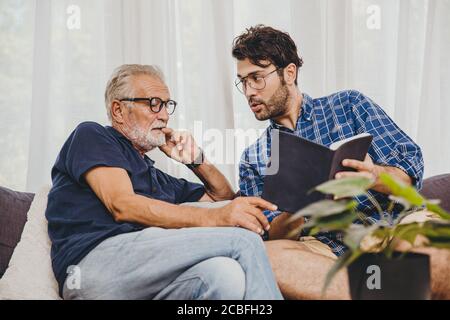 Young man consulting business project or education lecture content in text book with retired senior elder at home Stock Photo