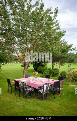 Table and chairs set for an outdoor summer party in a large garden with trees and shrubs. Rufford, Lancashire Stock Photo