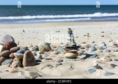 a pyramid of sea stones on the beach, sea stones are stacked on the sand Stock Photo