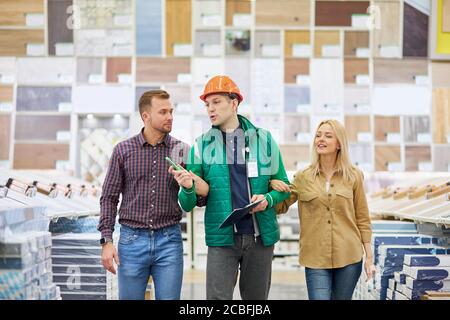 friendly staff in the market, married couple enjoy shopping, they hold worker's hand from both sides, going to make purchase, have conversation and ge Stock Photo
