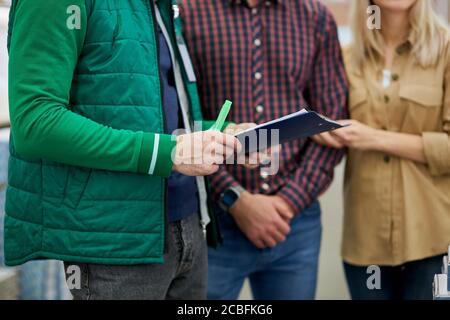 cropped manager of distribution center or warehouse worker help cutomers with choice, married couple came to make purchase in hypermarket, they doubt Stock Photo