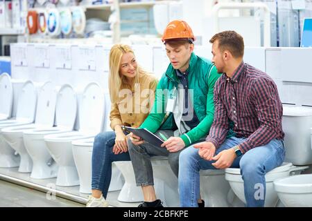 cute couple have conversation with warehouse worker sitting on toilet bowls in the market, caucasian worker is friendly staff Stock Photo
