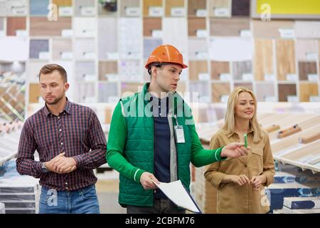 young caucasian married couple want to get commodity in the market, friendly warehouse worker help them with choose and advice, they have conversation Stock Photo
