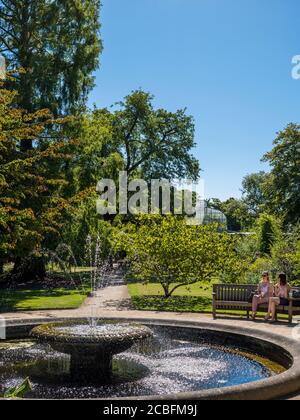 Two Young Woman Sitting Next to Pool with Fountain, University of Oxford Botanical Gardens, Oxford, Oxfordshire, England, UK, GB. Stock Photo