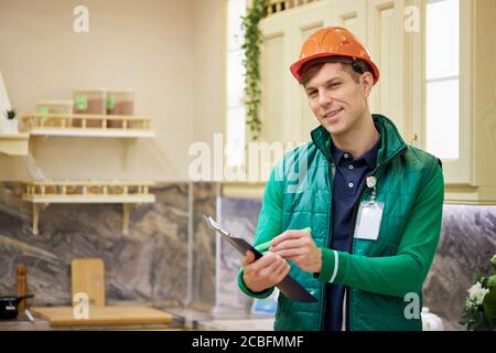 confident caucasian man warehouse worker check quantity of commodity in market, look on document and make notes if something is missing, smile and loo Stock Photo