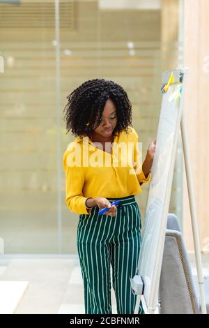beautiful woman in trendy clothes writing information on the flipchart. window in the background of the photo. close up shot. Stock Photo