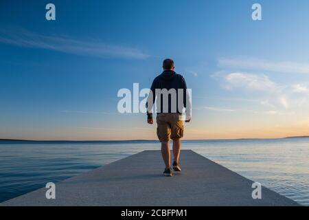 Man standing on long dock and watching sea horizon in sunset, island od Pag, Adriatic sea, Croatia, thoughtfulness concept Stock Photo