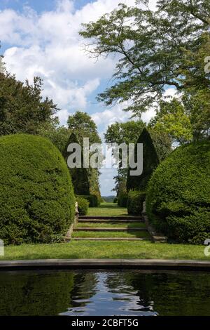 Landscape with formal garden, topiaries and reflecting pool under blue cloudy sky on beautiful sunny day Stock Photo