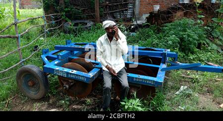 DISTRICT KATNI, INDIA - AUGUST 20, 2019: An indian village poor farmer man calling on phone while sitting upon tractor cultivator for asian people dig Stock Photo