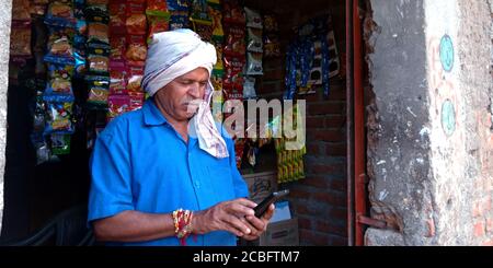 DISTRICT KATNI, INDIA - AUGUST 20, 2019: An indian village shopkeeper operating smart phone technology for asian traditional people digital learning c Stock Photo