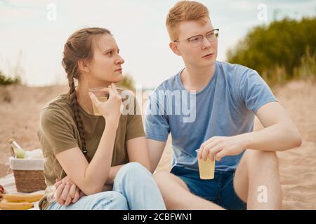 Teen couple looking away and having picnic on beach Stock Photo