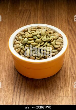 Green coffee beans in orange pot on wooden surface. Raw state before roasting. Stock Photo
