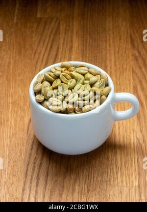 Green coffee beans in white espresso cup. Raw state before roasting. Stock Photo