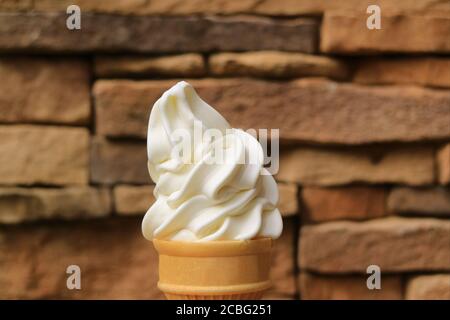 Mouthwatering Vanilla Soft Serve Ice Cream Cone Against Blurry Brown Stone Blocks Wall Stock Photo