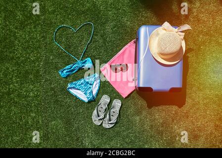 Luggage for summer vacations. Suitcase on grass with a towel and flip flops and sunglasses. Stock Photo