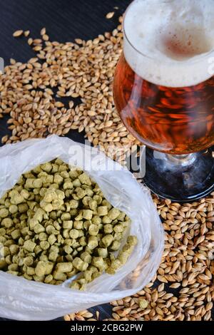 view of the components to make a frozen red or amber craft beer and the glass beer coup over a black wooden table Stock Photo