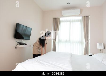 Young beautiful Asia maid arranging blanket on the bed in hotel room Stock Photo