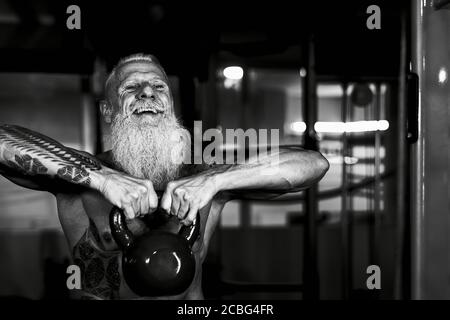 Senior fitness man doing kettle bell exercises inside gym - Fit mature male training in wellness club center Stock Photo