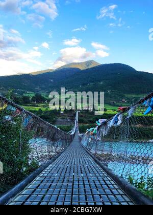 The Punakha Supsension Bridge at Punakha Dzong decked out with prayer flags before a mountainscape Stock Photo