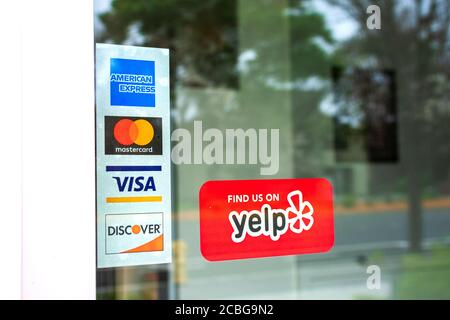 MasterCard, VISA, American Express, Discover payment options advertised on a restaurant door. A red sticker decal promotes Yelp crowd-sourced reviews Stock Photo
