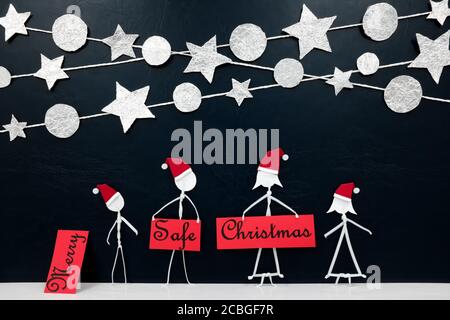 Family figure wearing santa hat holding a Safe Christmas greeting card with silver stars and balls ornament background. Covid Christmas celebration concept. Stock Photo