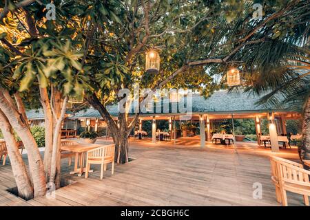 Outdoor restaurant at the beach during sunset, beautiful outdoor and indoor restaurant view in night candles illumination, wooden deck with chairs Stock Photo
