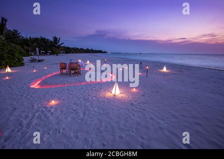 Amazing romantic dinner on the beach with chairs candles under sunset sky. Romance and love, luxury destination dinning, exotic table setup beach view Stock Photo