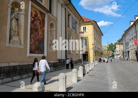 Ljubljana, Slovenia - July 16th 2018: Tourists walking past the art on the wall at Ljubljana Cathedral on Ciril-Metodov Trg, Slovenia Stock Photo