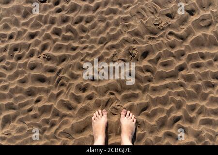 a close up view of the ripples in the sand from the low tide with someones feet Stock Photo