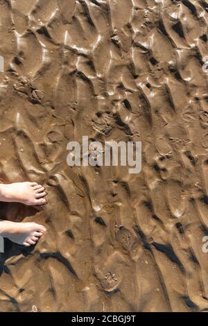 a close up view of the ripples in the sand from the low tide with someones feet Stock Photo