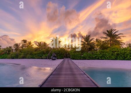 Sunset on Maldives island, luxury water villas resort and wooden pier. Beautiful sky clouds and palm tree beach background for summer vacation holiday Stock Photo