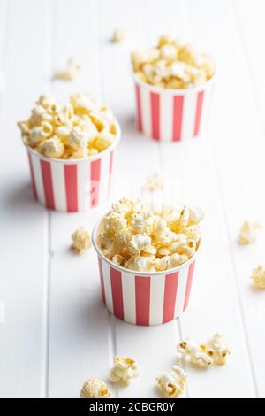 Sweet tasty popcorn in striped paper cup on white table. Stock Photo