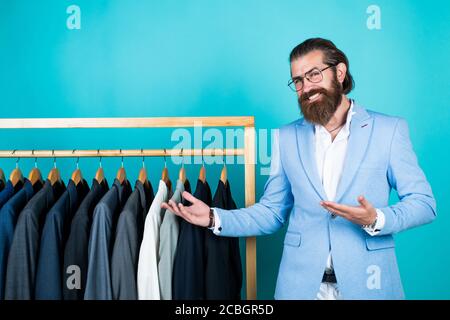 perfect design. tailor man has fashionable look. Elegant suits hang in row. Mens clothes on hanger. mature man looking for jacket. professional male sartor with jacket on hanger. presenting product. Stock Photo
