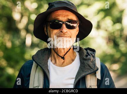 Portrait of a senior man carrying a backpack wearing a hat and glasses looking at camera Stock Photo