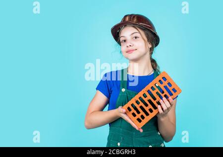 building her future house. happy childhood. kid wear protective helmet. protect head on construction site. teen girl hold brick. little builder with brick. Stock Photo
