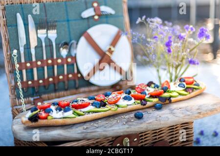 Stylish summer picnic set up, with a picnic hamper and vegetarian baguette of avocado, tomatoes and mozarella cheese