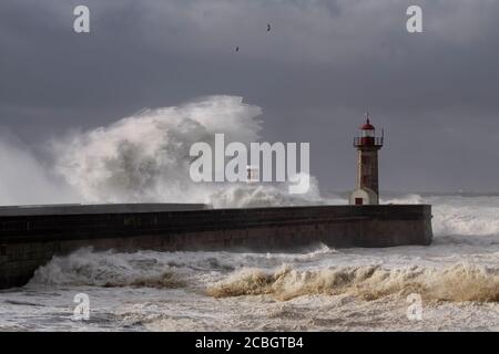 Big white waves over piers and lighthouse against a dark cloudy sky before rain. Douro river mouth, Porto, Portugal, during sea storm. Stock Photo