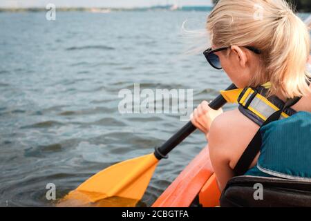 Close up and back view of young blond woman kayaking on the river in sunny summer day. Nice time for kayaking. Close up, back view Stock Photo