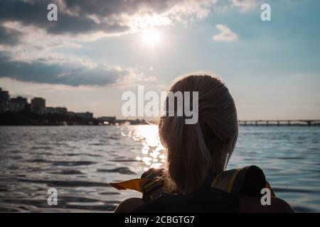 Back view and close up of young woman looking at sunset while kayaking on the river in summer. Nice time for kayaking. Close up Stock Photo
