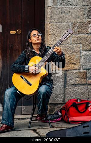 Barcelona, Spain 05/01/2010: A young woman is sitting on a stool in the street and playing classical guitar. This street performer is in the historic Stock Photo