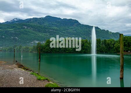 Landscape photo of a mountain lake amongst Swiss Alps. The long exposure photo features a water jet fountain in the  lake ejecting high pressure water Stock Photo