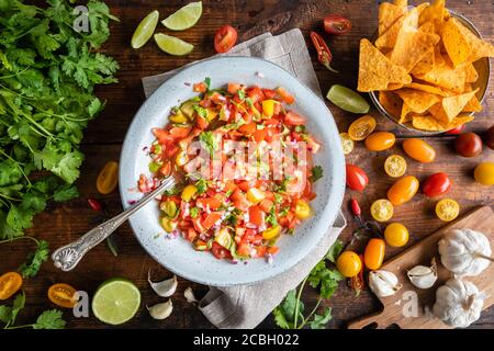 Tex Mex Pico de Gallo with nacho tortilla chips. The bowl of tomato salsa is seen from above, flat lay, and there are typical ingredients such as scat Stock Photo