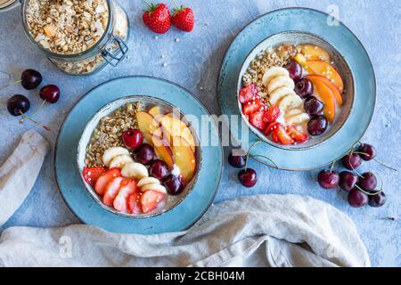 A healthy breakfast yogurt meal with fresh fruit, granola and puffed quinoa. The blue gray bowls are filled with  strawberries, peaches, banana and ch Stock Photo