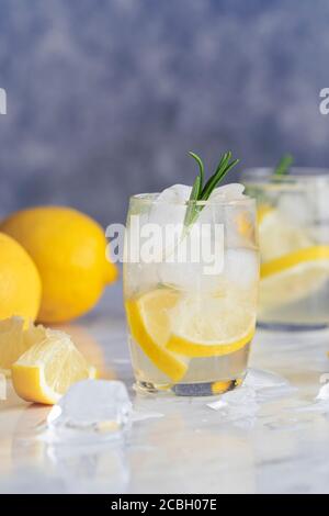 Lemon drink with rosemary and ice. Concept gin and tonic, GT. On a rustic wooden background. Refreshing cocktail or detox mocktail with homegrown herb