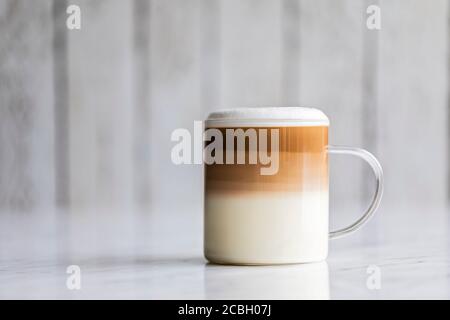 Cafe latte macchiato layered coffee in a see through glass coffee cup. The cup has a white wooden background. Stock Photo