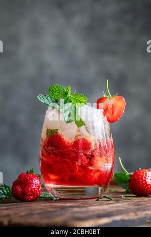 A fresh strawberry mojito drink. The cocktail or mocktail is on a vintage wooden dark table. The drink is decorated with strawberries and fresh mint. Stock Photo