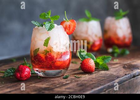 Fresh strawberry mojito drinks. There are three drinks on a vintage wooden dark table.  The cocktails or mocktails are decorated with strawberries and Stock Photo