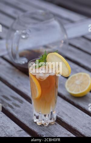 A glass of ice tea with lemon and mint, on a rustic gray aged table with a glass tea pot in the background and half a lemon. Vertical shot with copy s Stock Photo