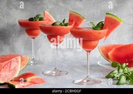Three  fresh frozen blended margarita drinks with strawberries and watermelon. The drinks are garnished with basil leaves and watermelon. Gray backgro Stock Photo