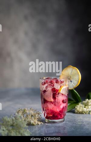Elderberry drink with pomegranate, lemon and ice. Fresh pink summer lemonade. Decorated with fresh elderberry flowers. On a gray background with copy Stock Photo